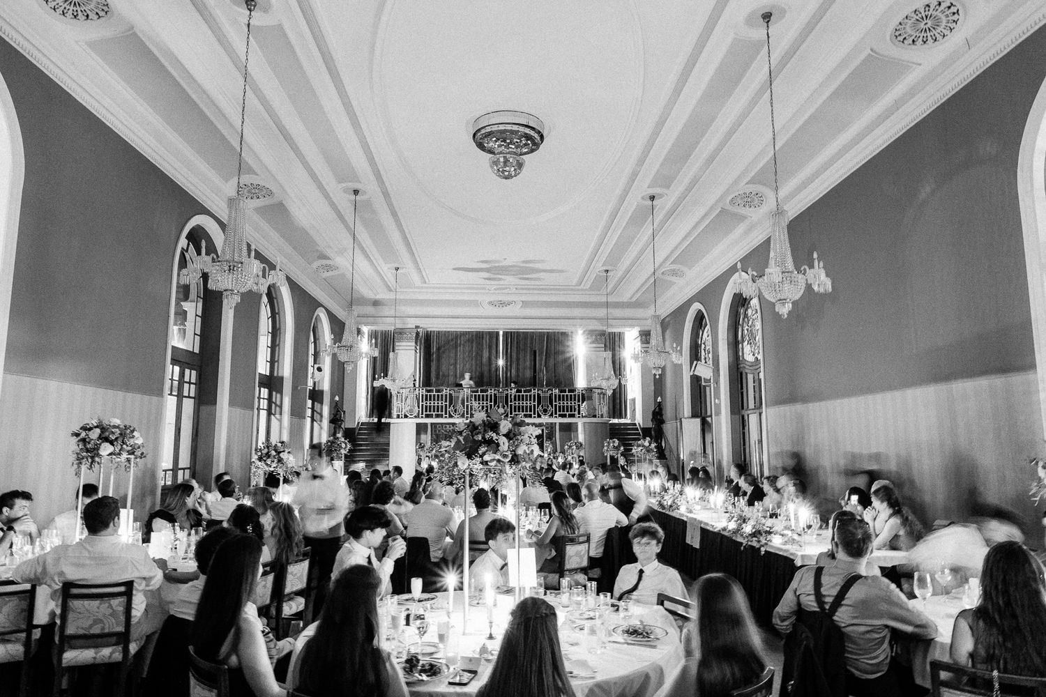 Elegant black and white photo of a grand banquet hall filled with guests dining at round tables during a formal event.