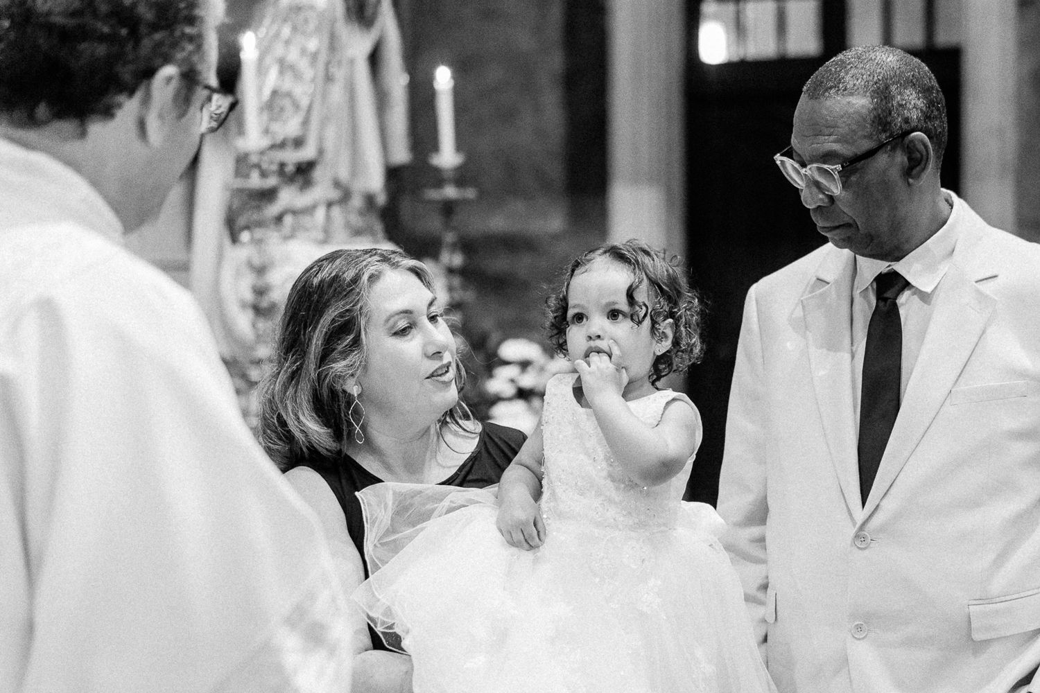 Black and white photo of a woman holding a child in a white dress during a church baptism ceremony.