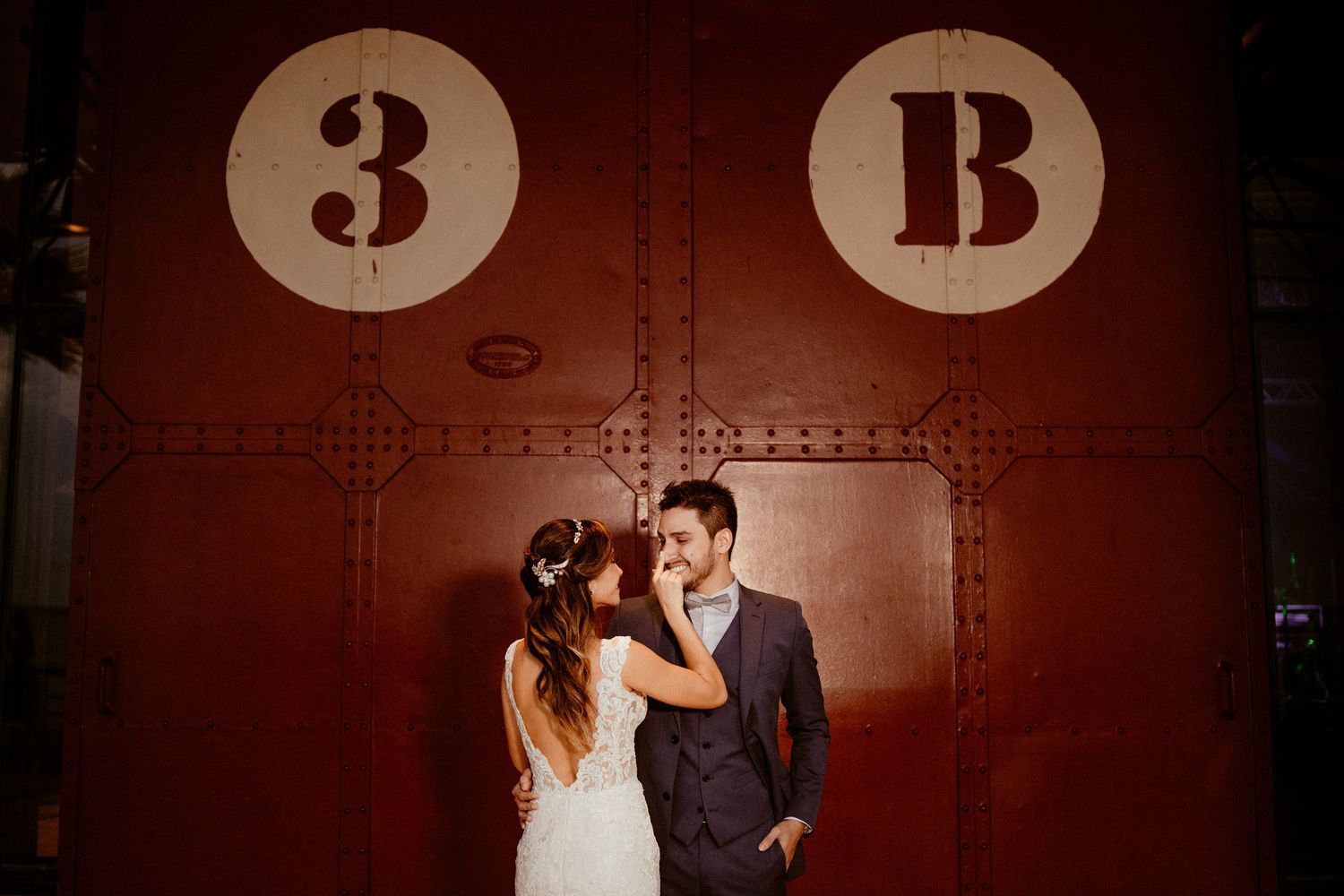 Silhouetted figures dance and pose together against dark red atmospheric lighting at a wedding reception venue.