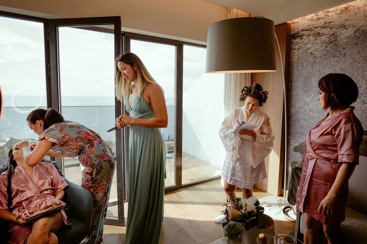 A series of bridesmaids getting ready in a sunlit room wearing pastel and mauve dresses for a wedding day celebration.