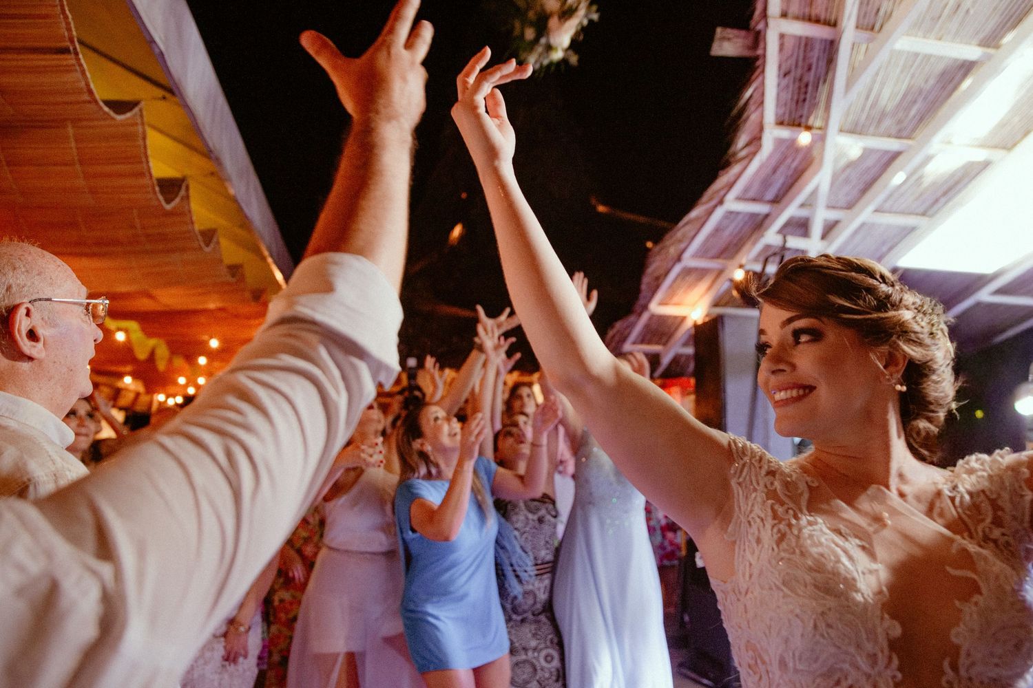 Wedding celebration with guests dancing and high-fiving on a festively lit dance floor.
