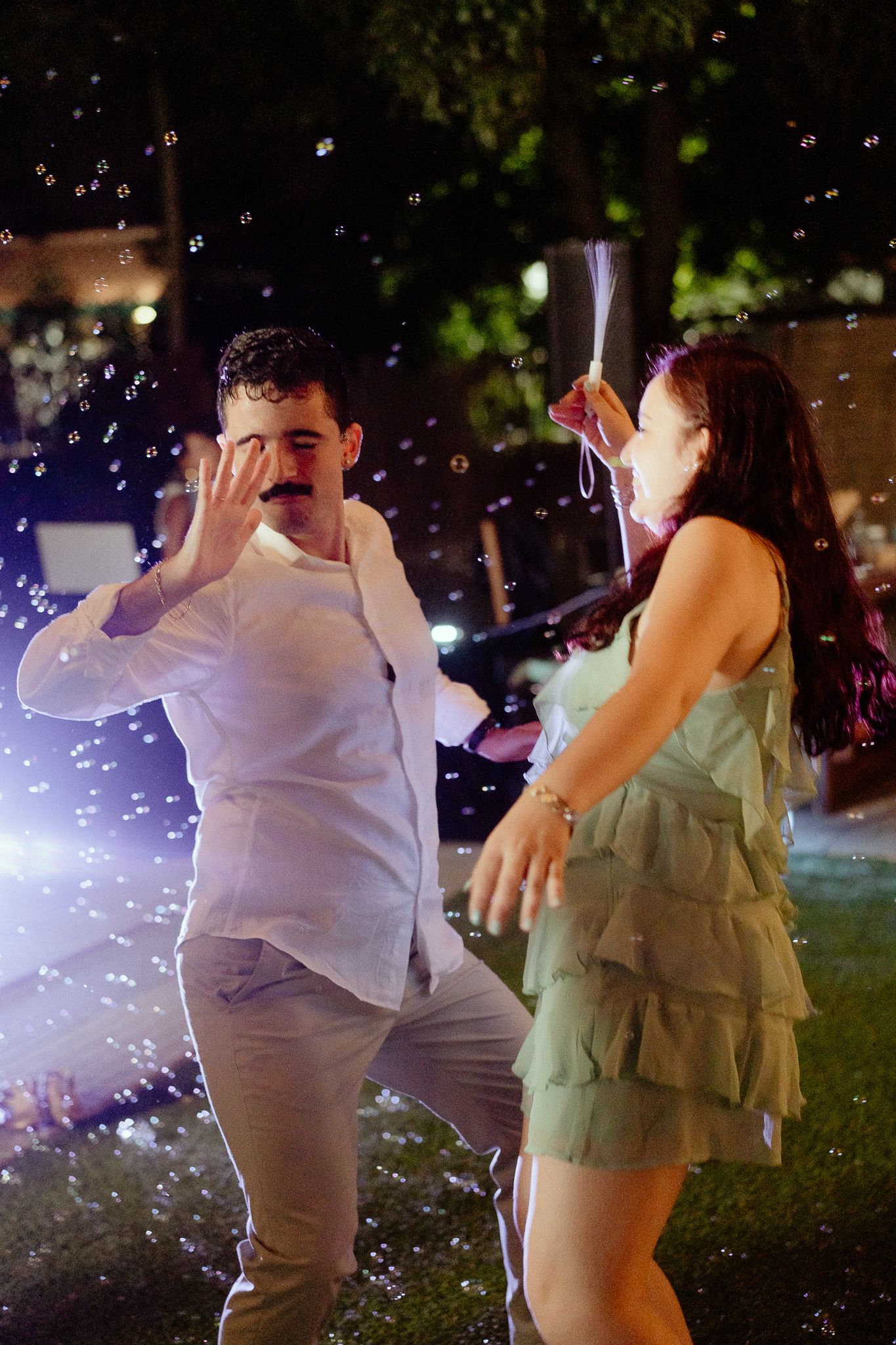 A man and woman dancing outdoors at night surrounded by floating soap bubbles at a festive party.