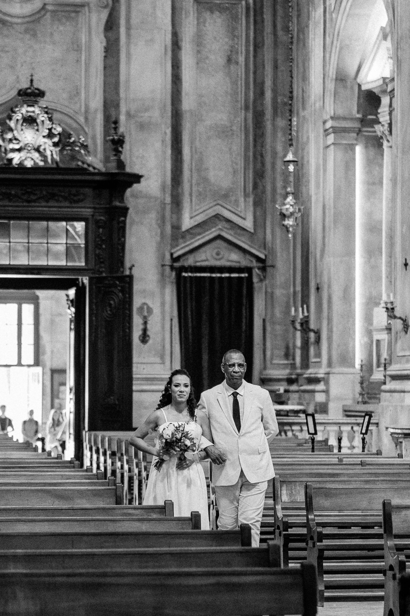Black and white photo of a bride and groom walking down the aisle of an elegant church during their wedding ceremony.
