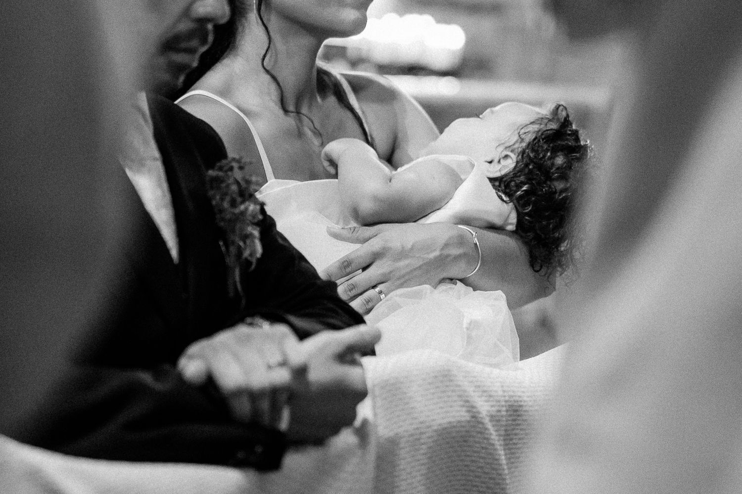 Black and white photo of a woman holding a baby during a baptism ceremony in a church.