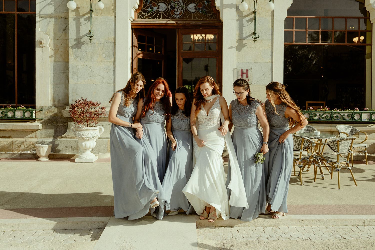 Bride and bridesmaids in gray dresses walking together outside a elegant wedding venue.