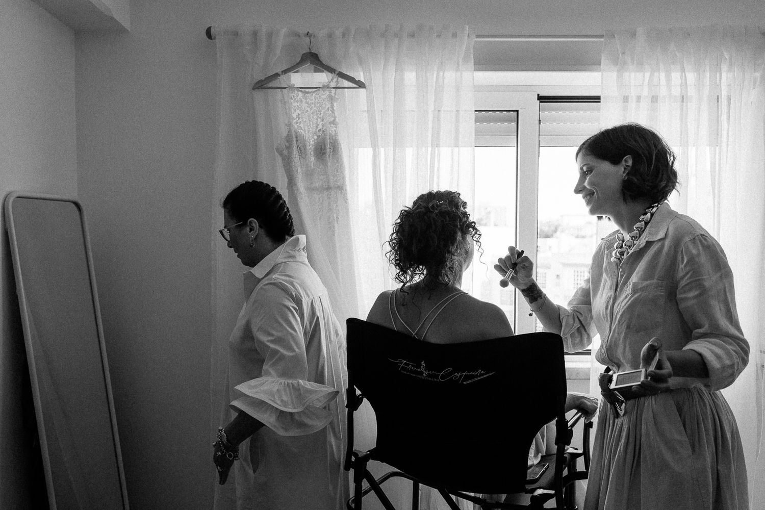 Black and white photo of a bride getting ready, with attendants helping her before the wedding ceremony.