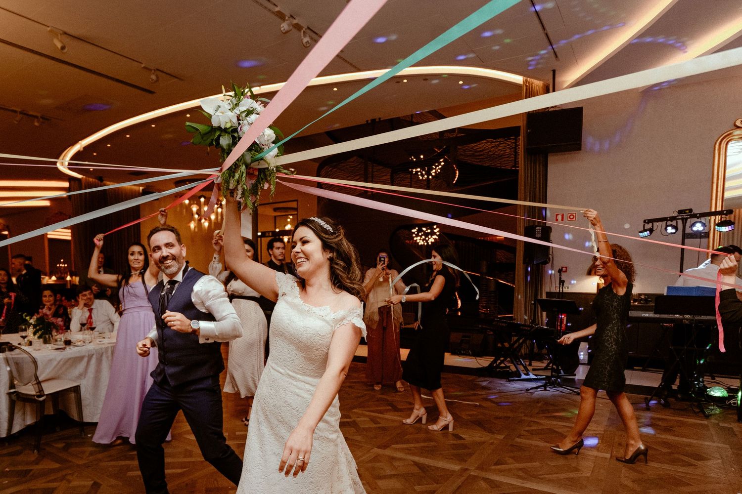 Wedding reception dance party scene with guests celebrating under decorative geometric light fixtures at an indoor venue.