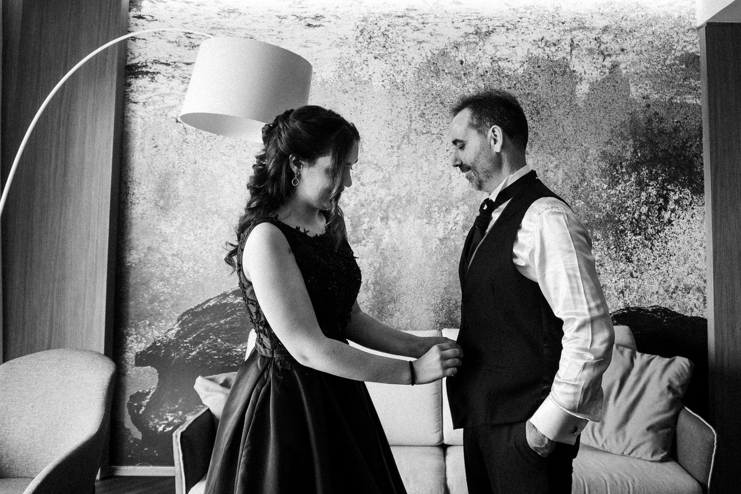 Two people in an intimate monochrome dance pose against a textured wall in dramatic lighting.