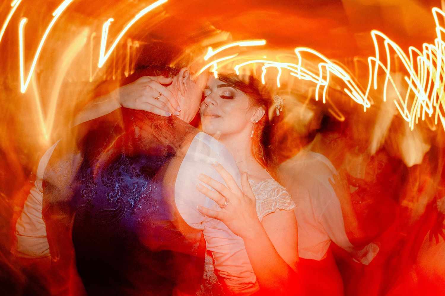Abstract motion blur photograph of dancing at a wedding reception with orange light trails.