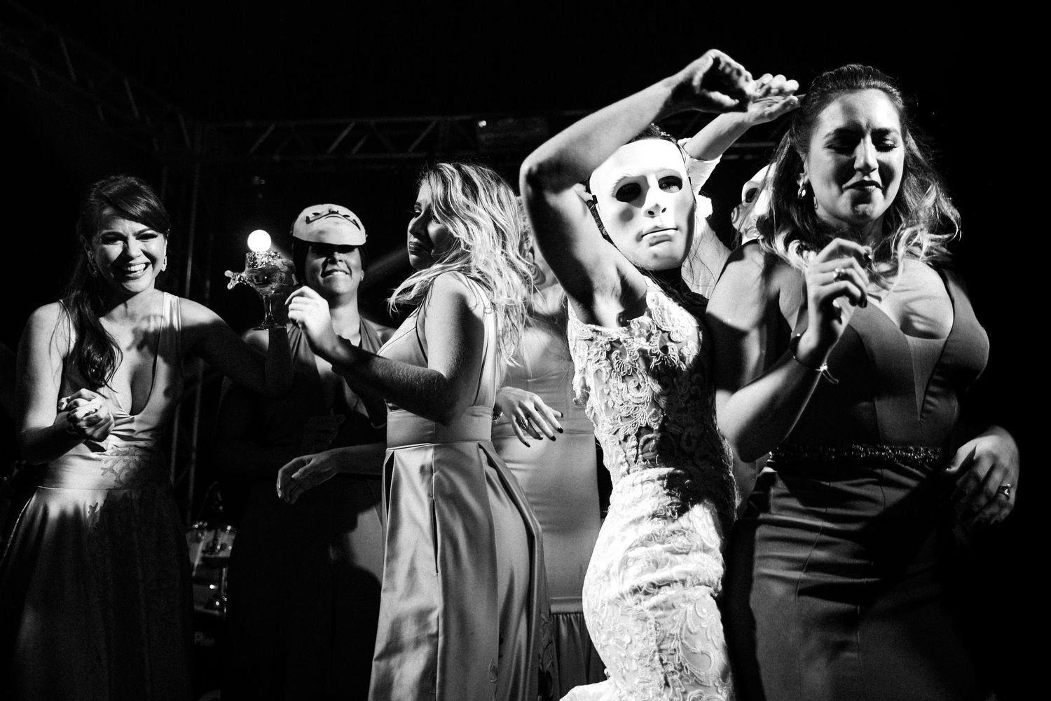 A black and white photo captures wedding guests dancing enthusiastically at a lively reception party.