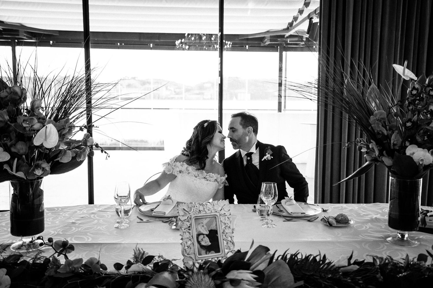 Black and white photo of newlyweds sharing romantic moment at decorated reception table.
