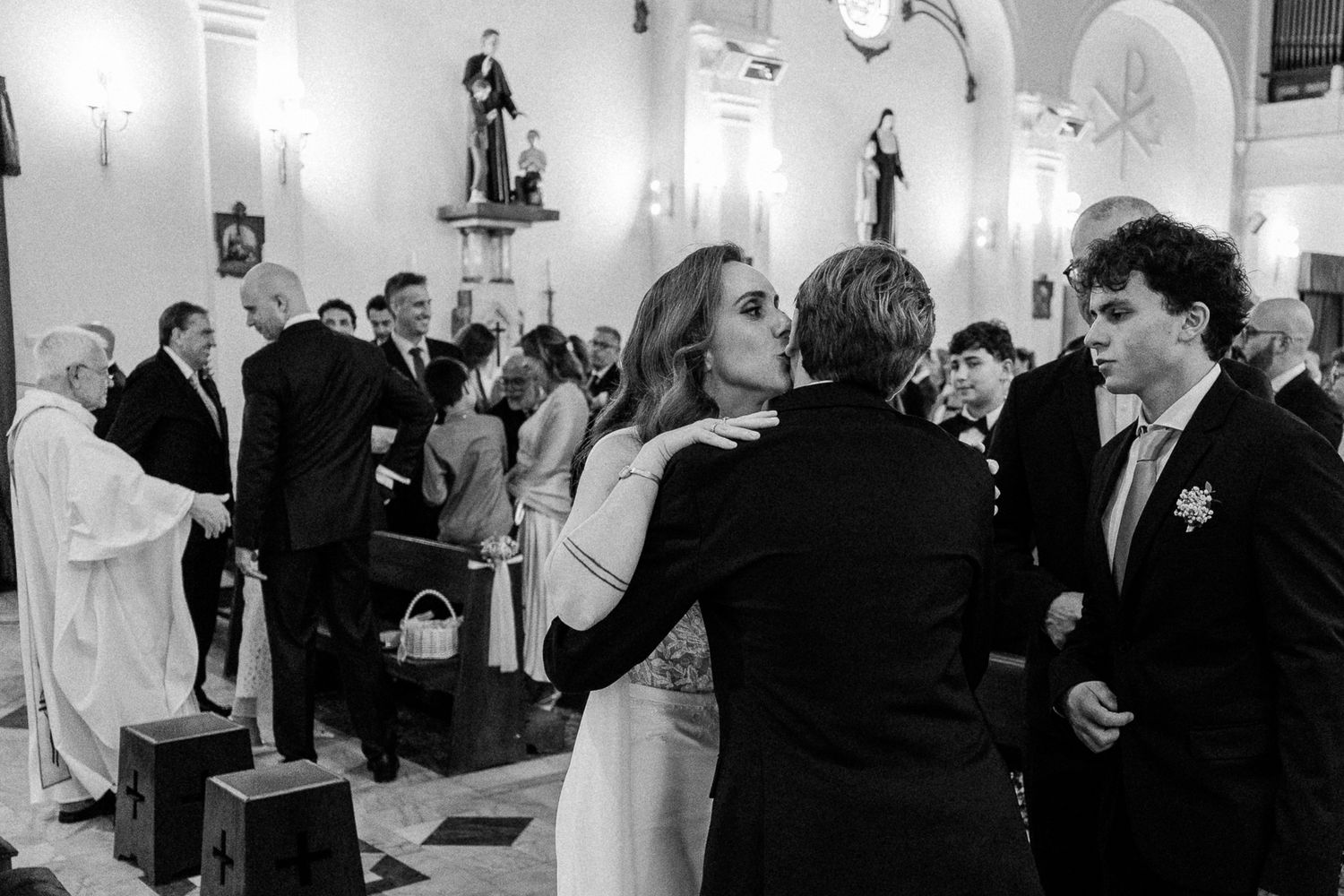 Black and white wedding photo of guests embracing and congratulating the bride inside a church.