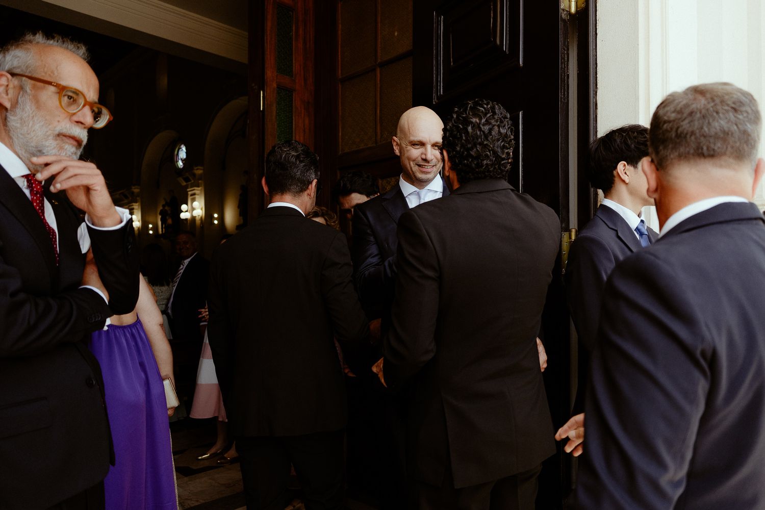 Elegantly dressed guests mingling outside a formal venue during a sophisticated social gathering or wedding reception.