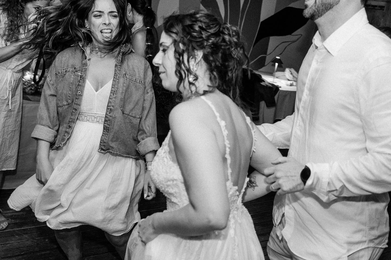 Black and white photo of bride dancing joyfully with guests at a lively wedding reception celebration.