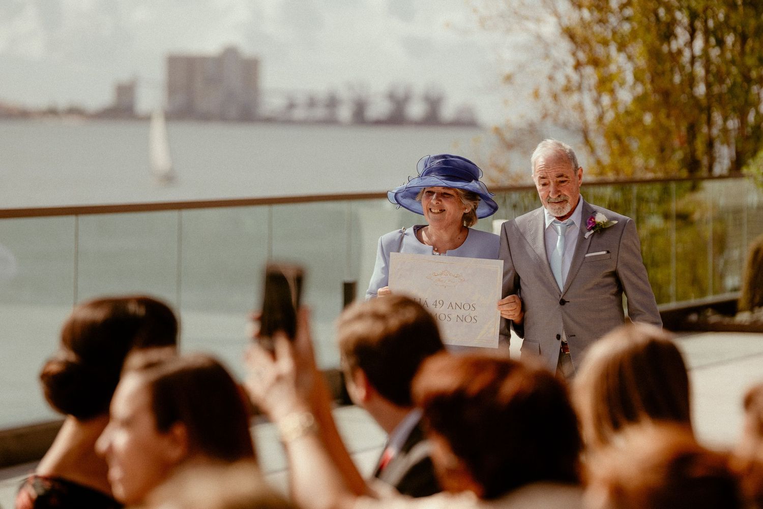 Wedding ceremony guests watching attentively during an outdoor celebration near a waterfront setting at sunset.