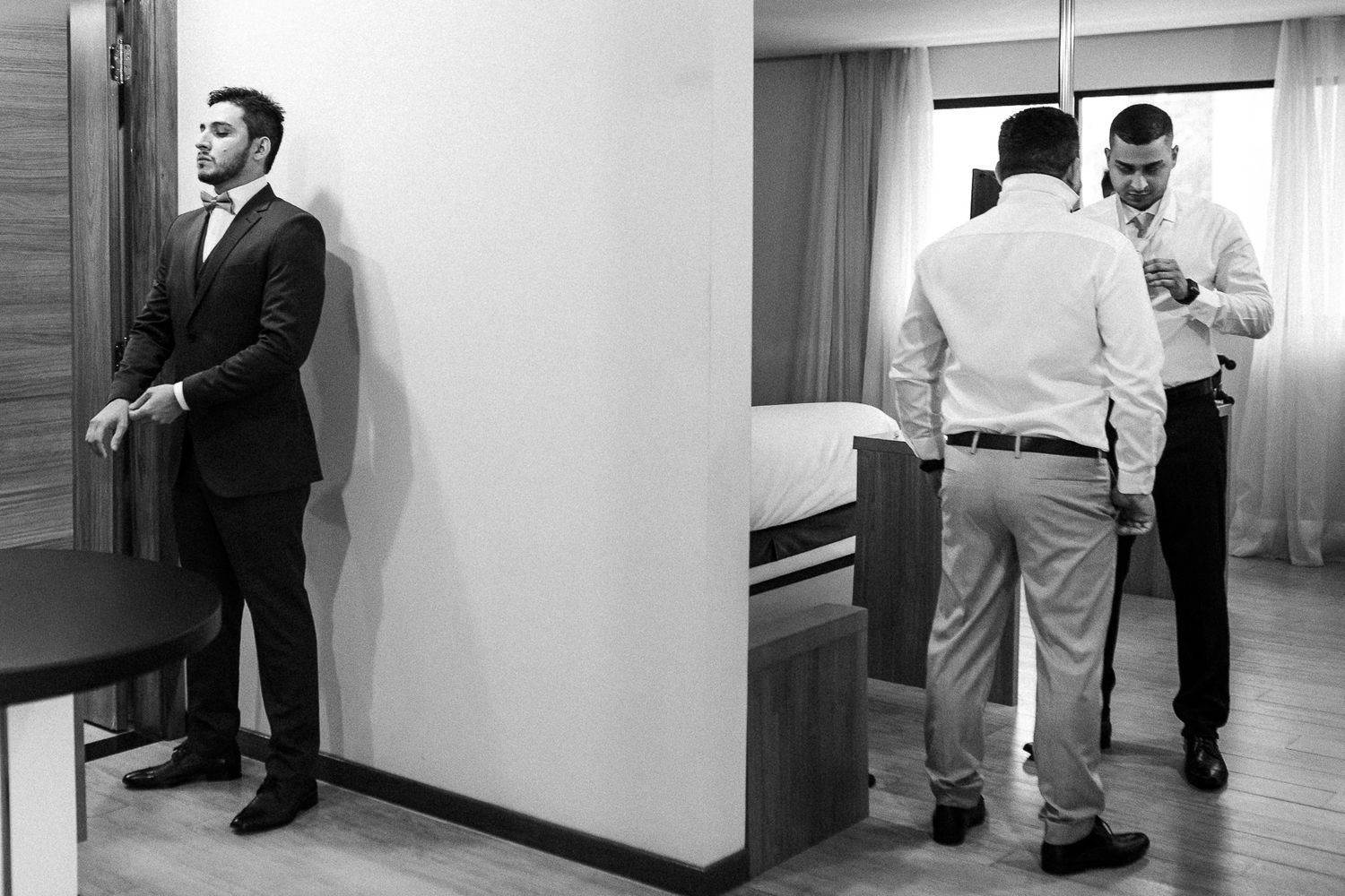 Black and white photo showing a groom getting ready before a wedding in a hotel room.
