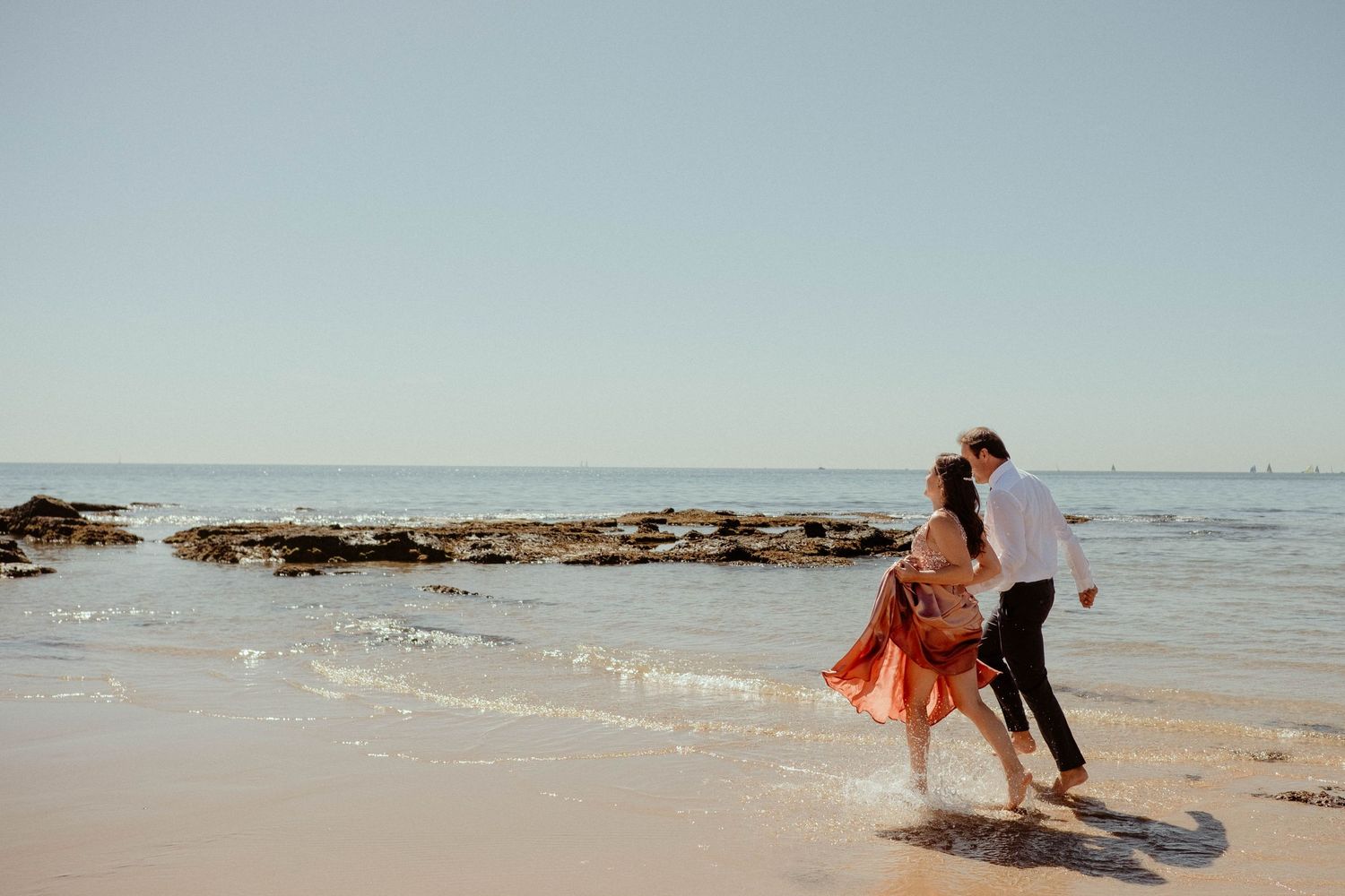 A person in a coral dress walks along a sandy beach at sunset with waves crashing in the background.