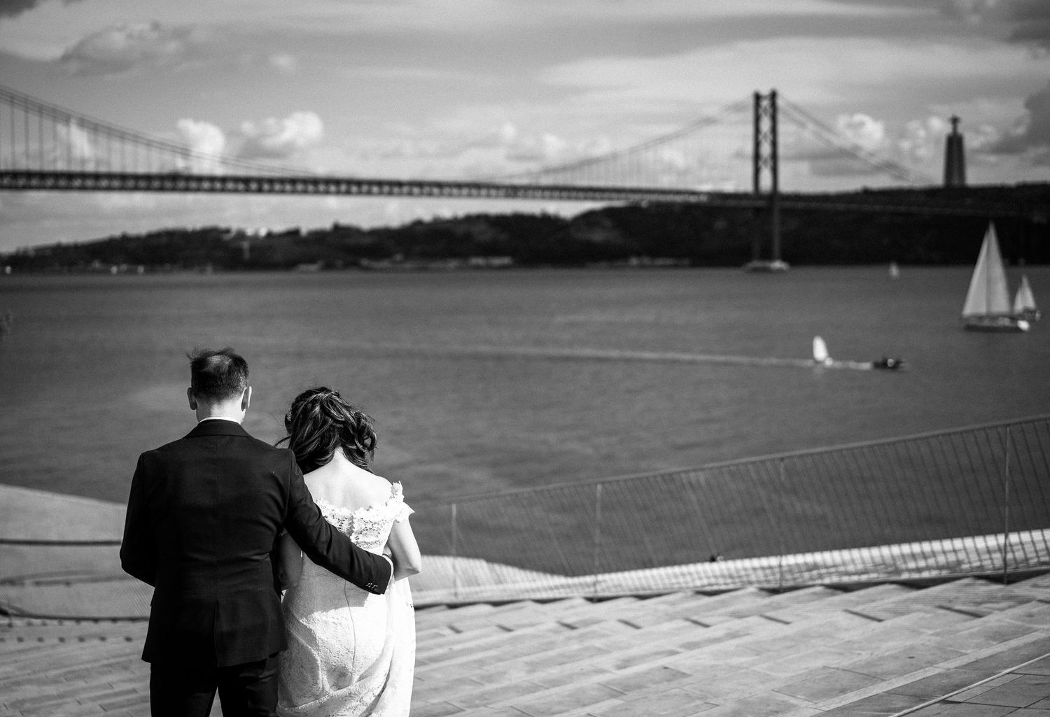 A couple admires the view of the 25th of April Bridge in Lisbon from a scenic overlook.