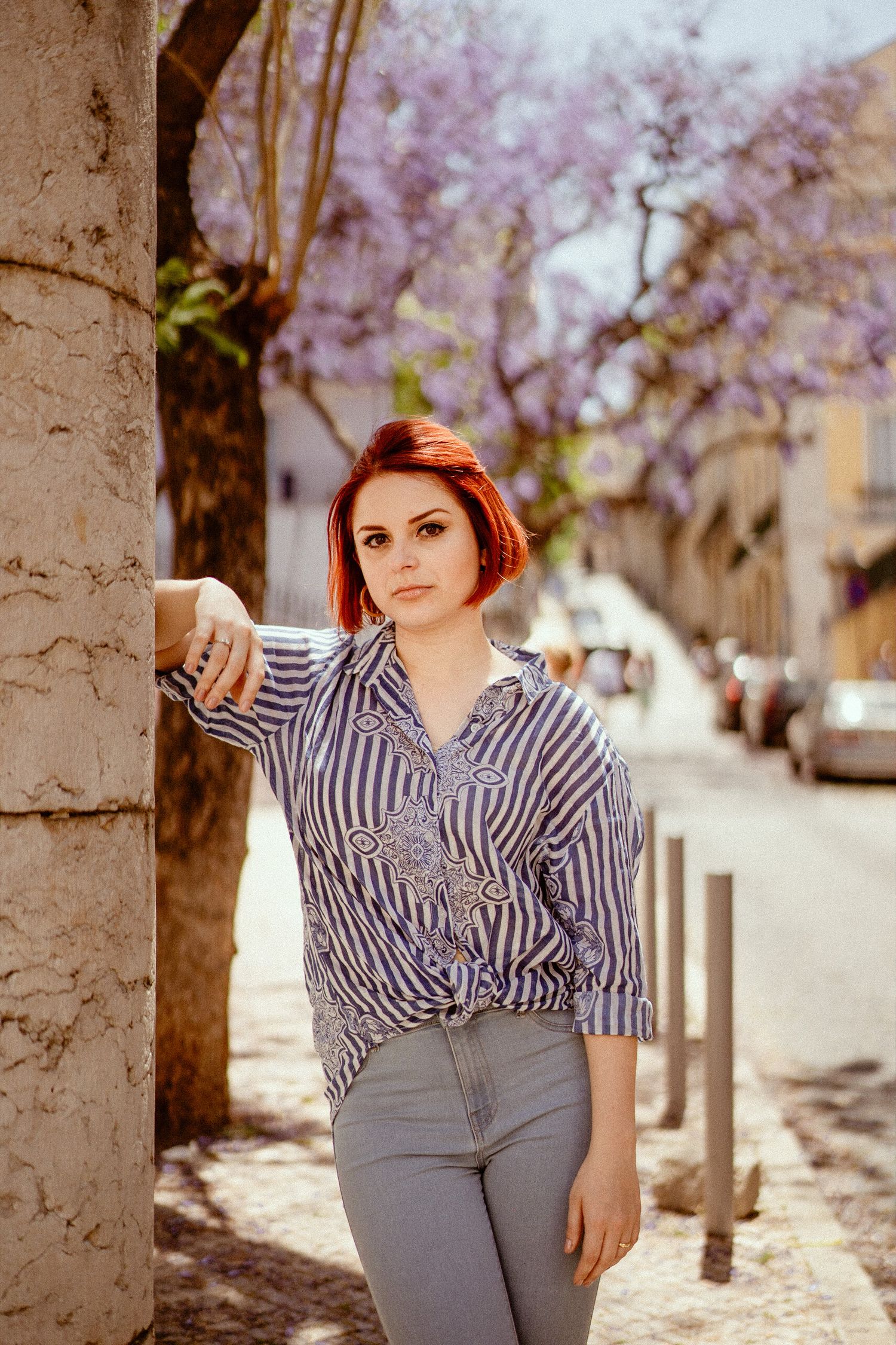 Casual street style portrait in striped shirt against blooming purple trees.