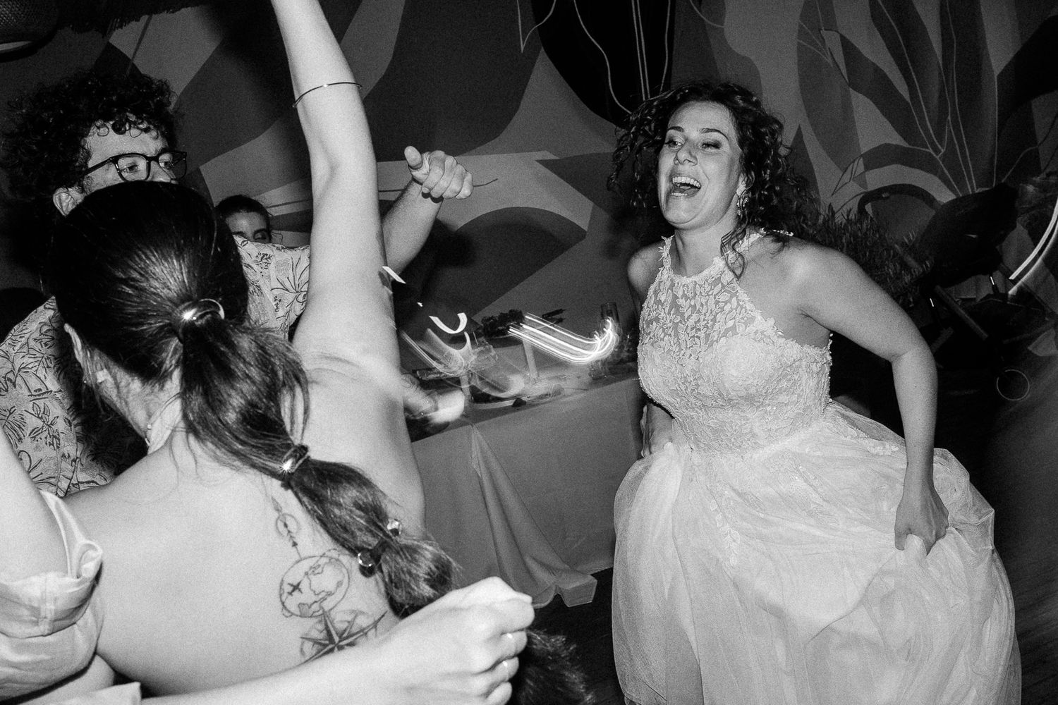 Bride dancing joyfully with guests at wedding reception in black and white photo.