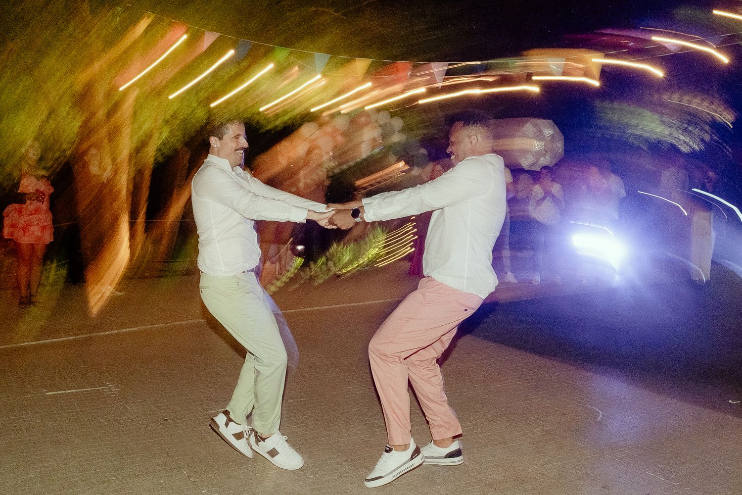 Two people dancing energetically outdoors at night with colorful light trails and motion blur in background.