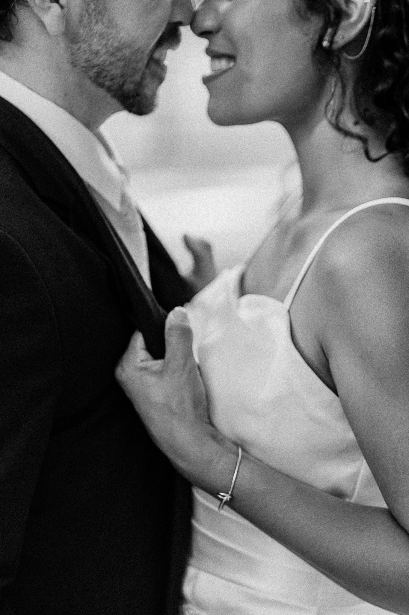Black and white photo of a bride and groom in an intimate moment, her hand on his chest, wearing a satin dress.