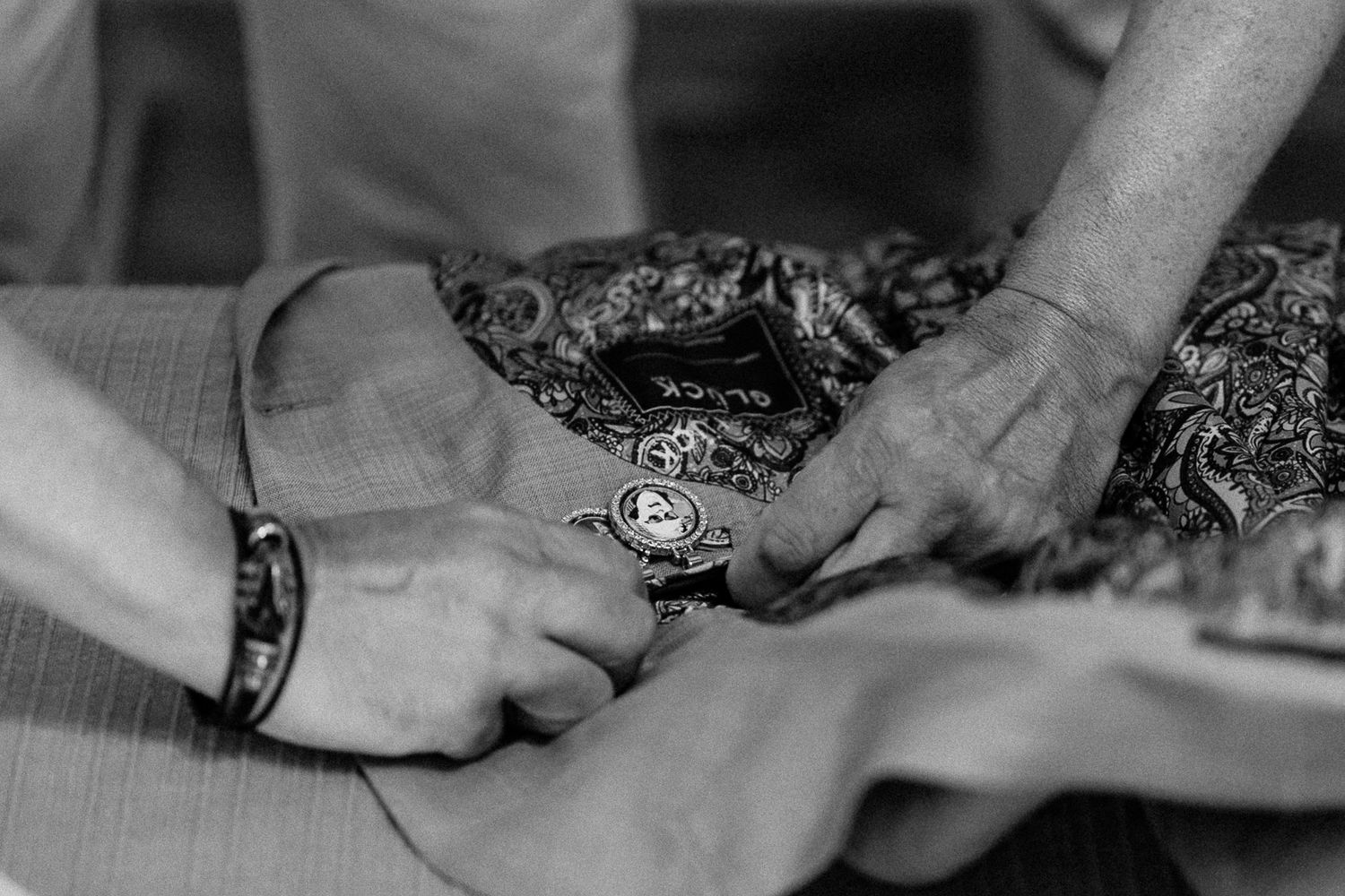 Close-up of hands adjusting a floral fabric garment on a table, captured in black and white.