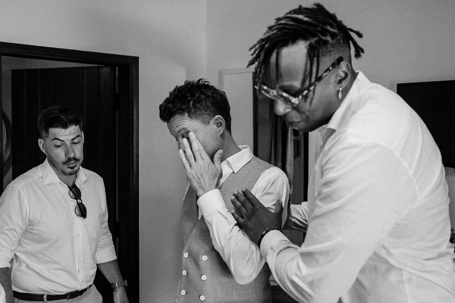 Black and white photo of groomsmen helping emotional groom prepare before wedding ceremony.