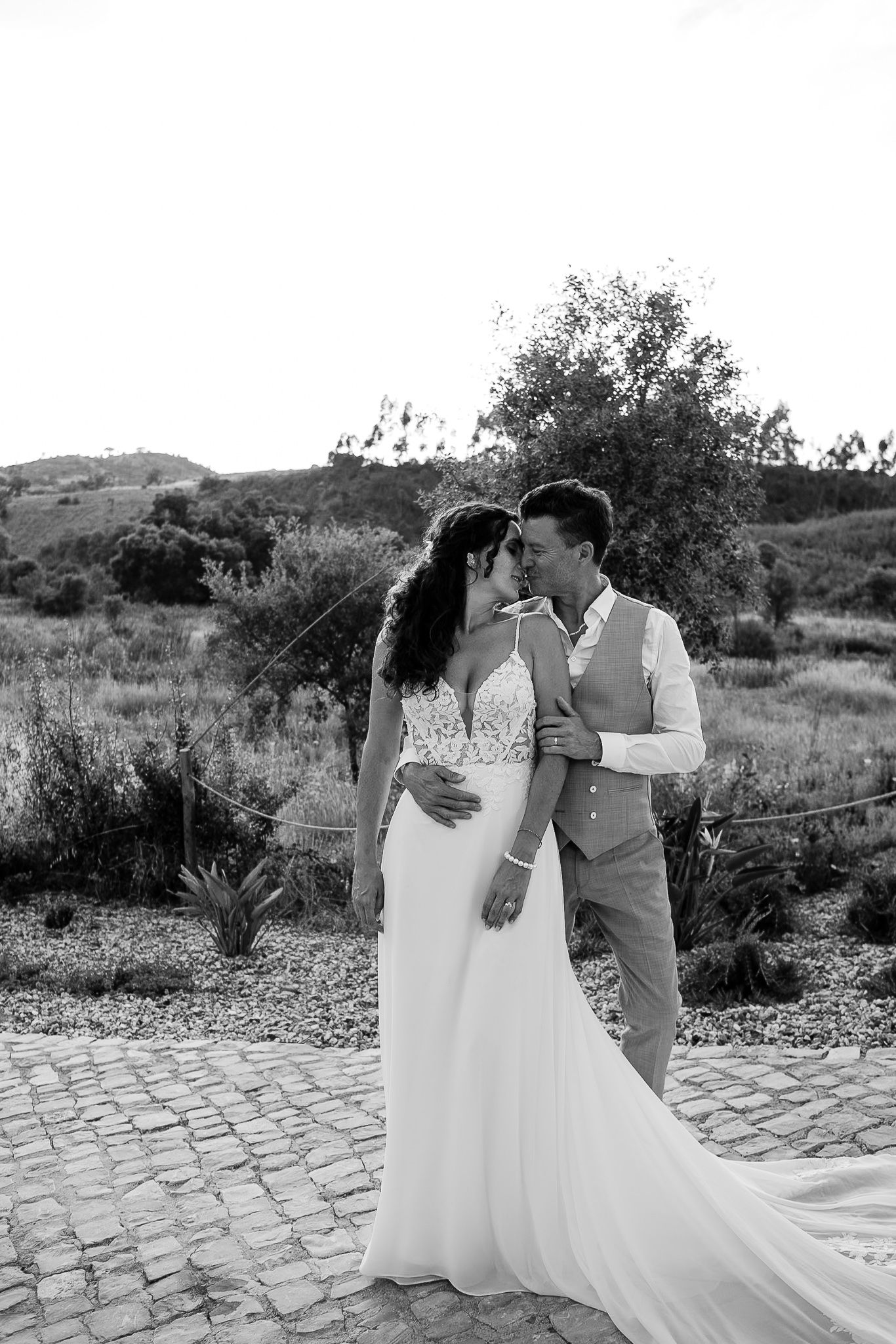 Black and white photo of a bride and groom sharing a romantic moment outdoors on a cobblestone path.