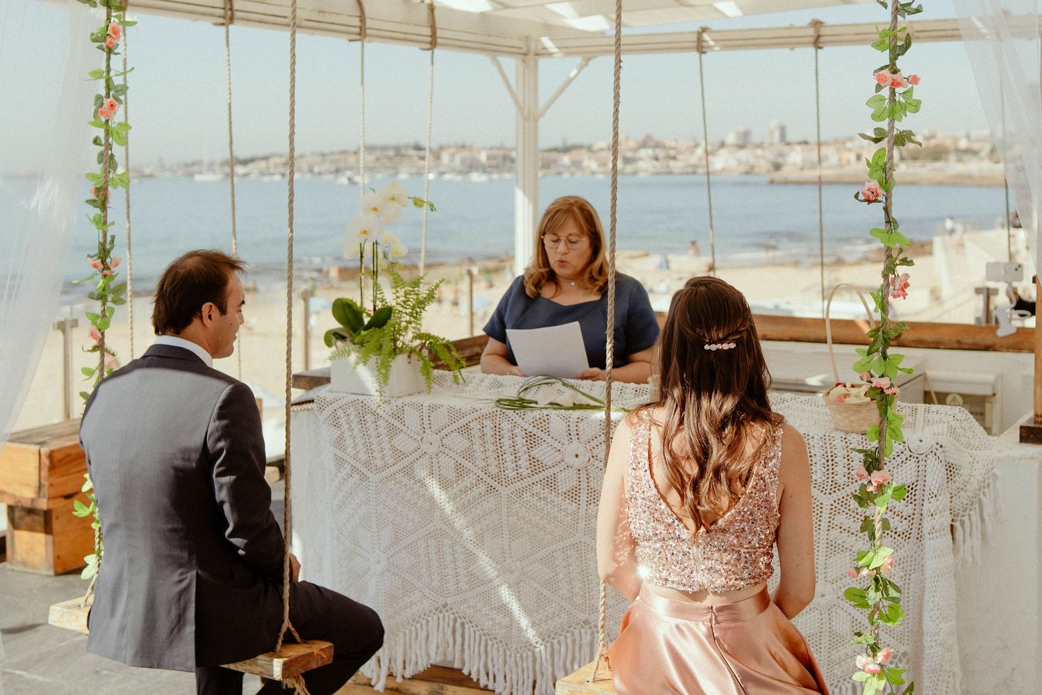 A romantic rooftop wedding ceremony setup with hanging greenery and white decor overlooking a waterfront cityscape.