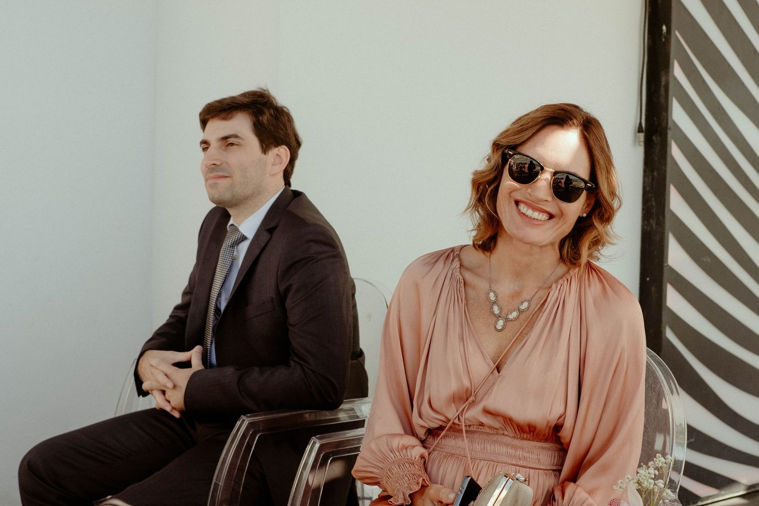 Professional group in business attire poses together against a gray striped wall background.