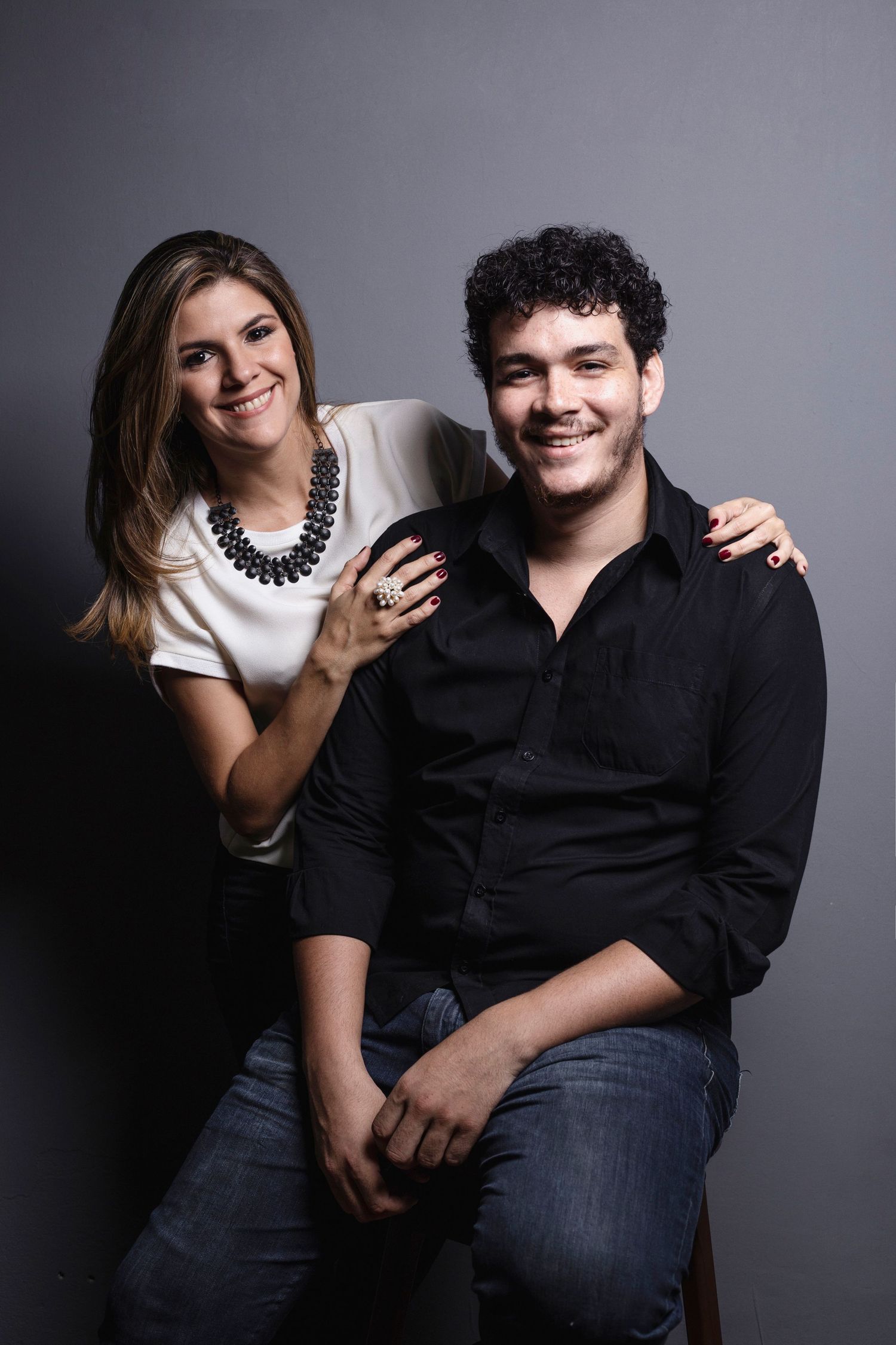 A couple in dark and white attire poses playfully against a gray background in a series of candid studio shots.