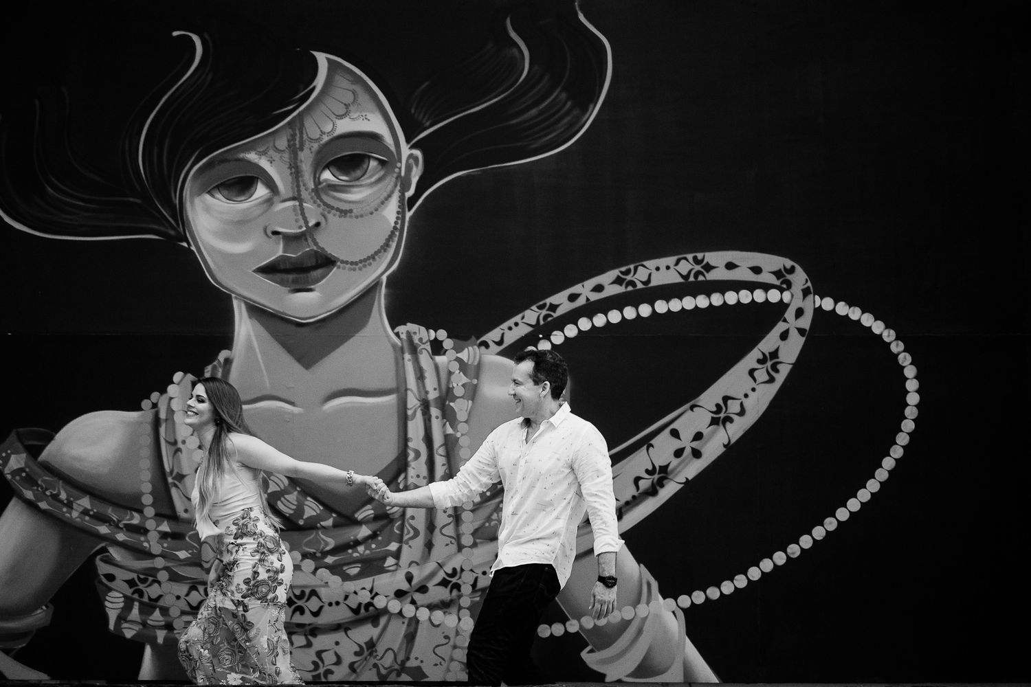 Black and white artistic photograph showing a person standing in front of a large illuminated mural artwork.