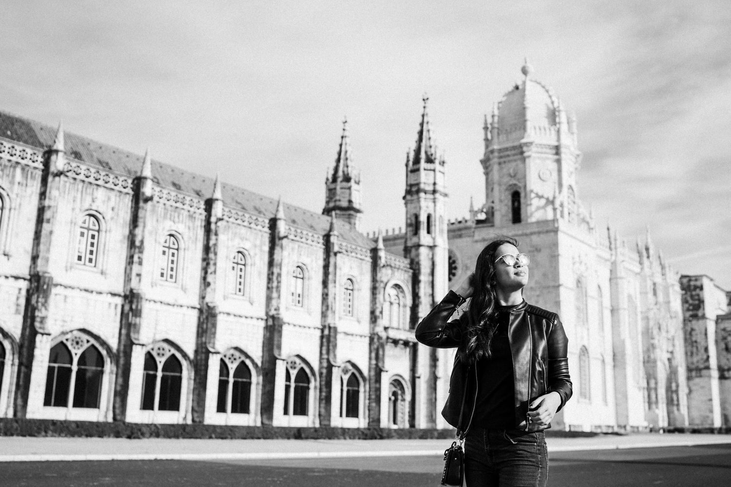 A person in dark clothing stands before the majestic Jeronimos Monastery in Lisbon.