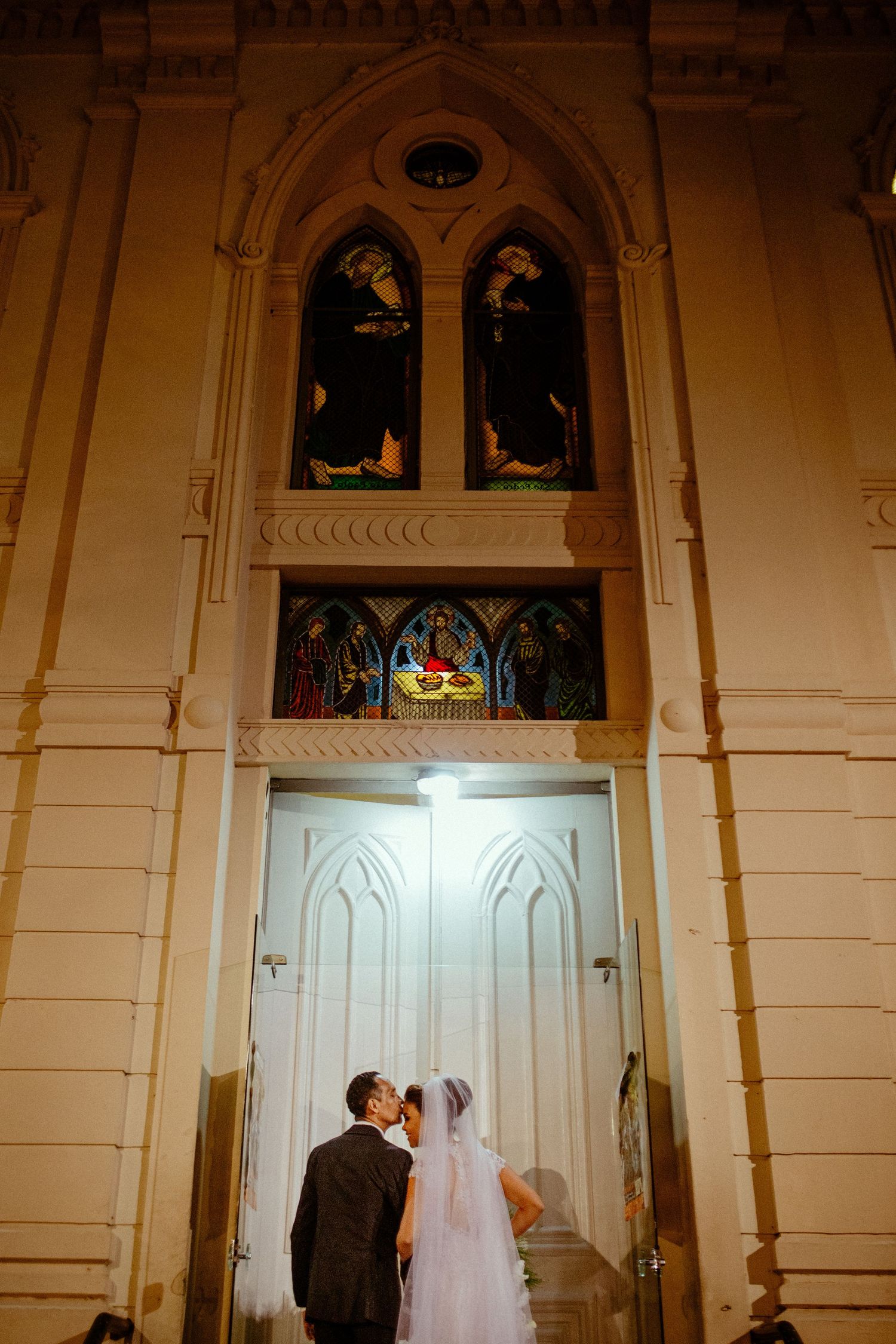Newlyweds standing in front of grand cathedral doors beneath Gothic arched windows.