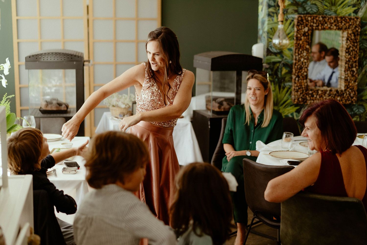 A group of people gather around a table in a bright, sunlit room during what appears to be a social gathering.
