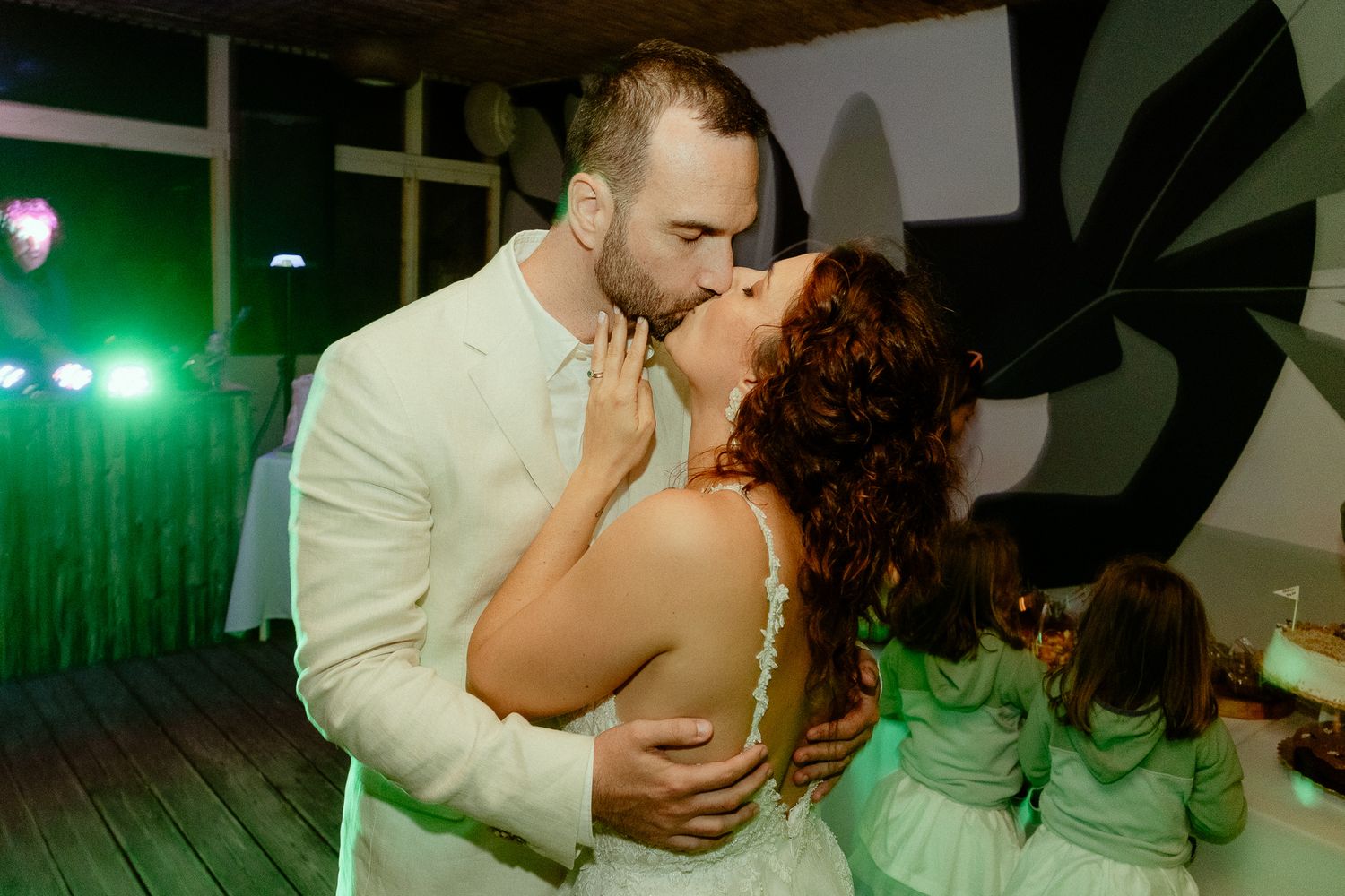 Bride and groom sharing a romantic first dance kiss at their wedding reception with green lighting.