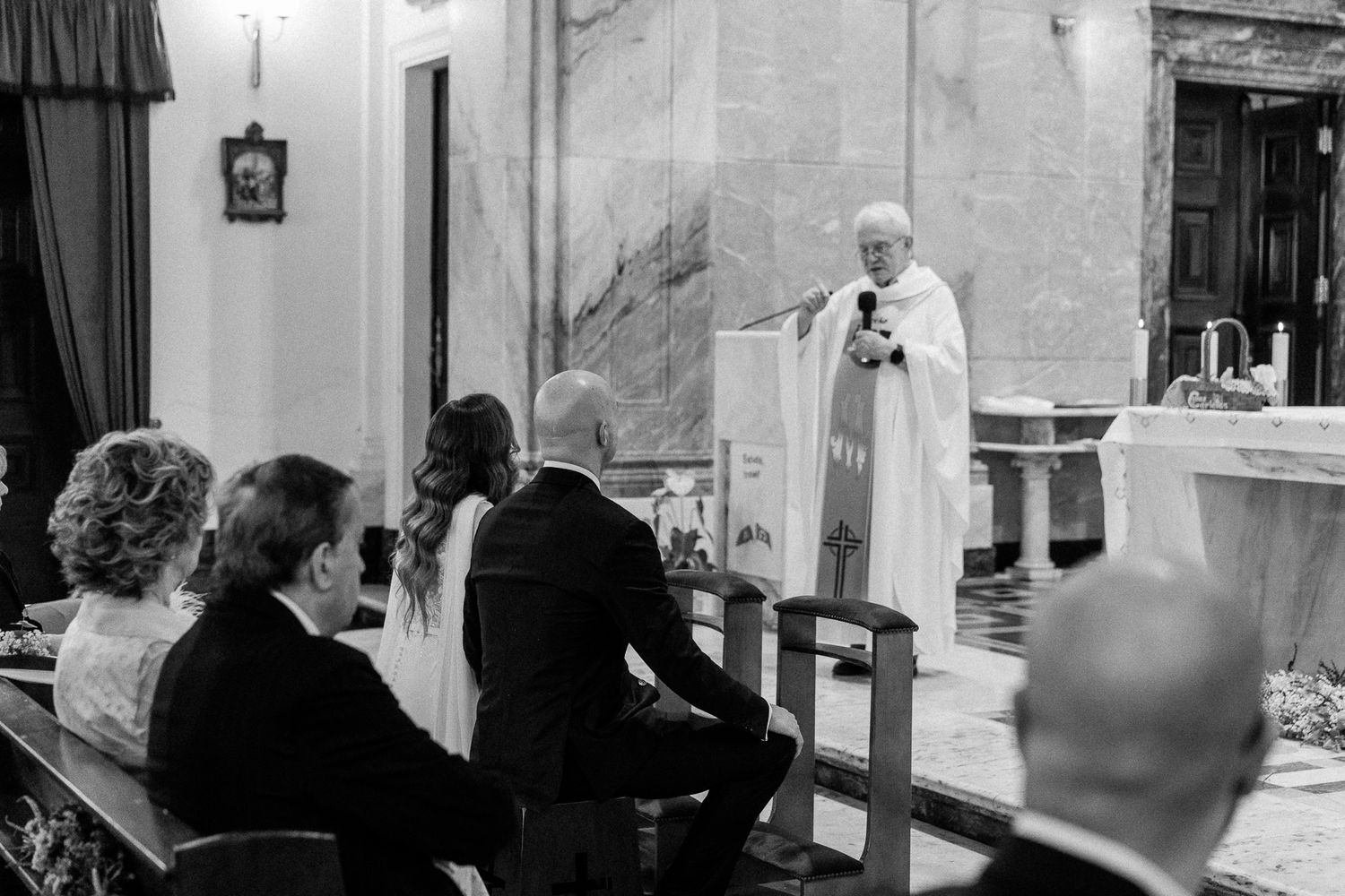 Black and white photo of a priest officiating a wedding ceremony at the altar with guests seated in church pews.