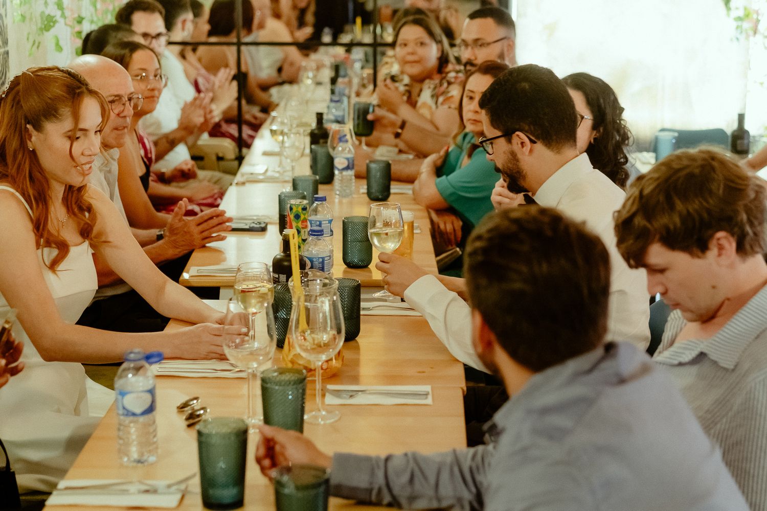 Guests enjoying a lively dinner party seated at a long wooden table with wine glasses and candles.