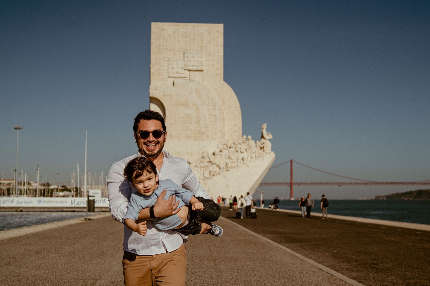Standing by the iconic Monument to the Discoveries in Lisbon, Portugal with the April 25th Bridge in the background.