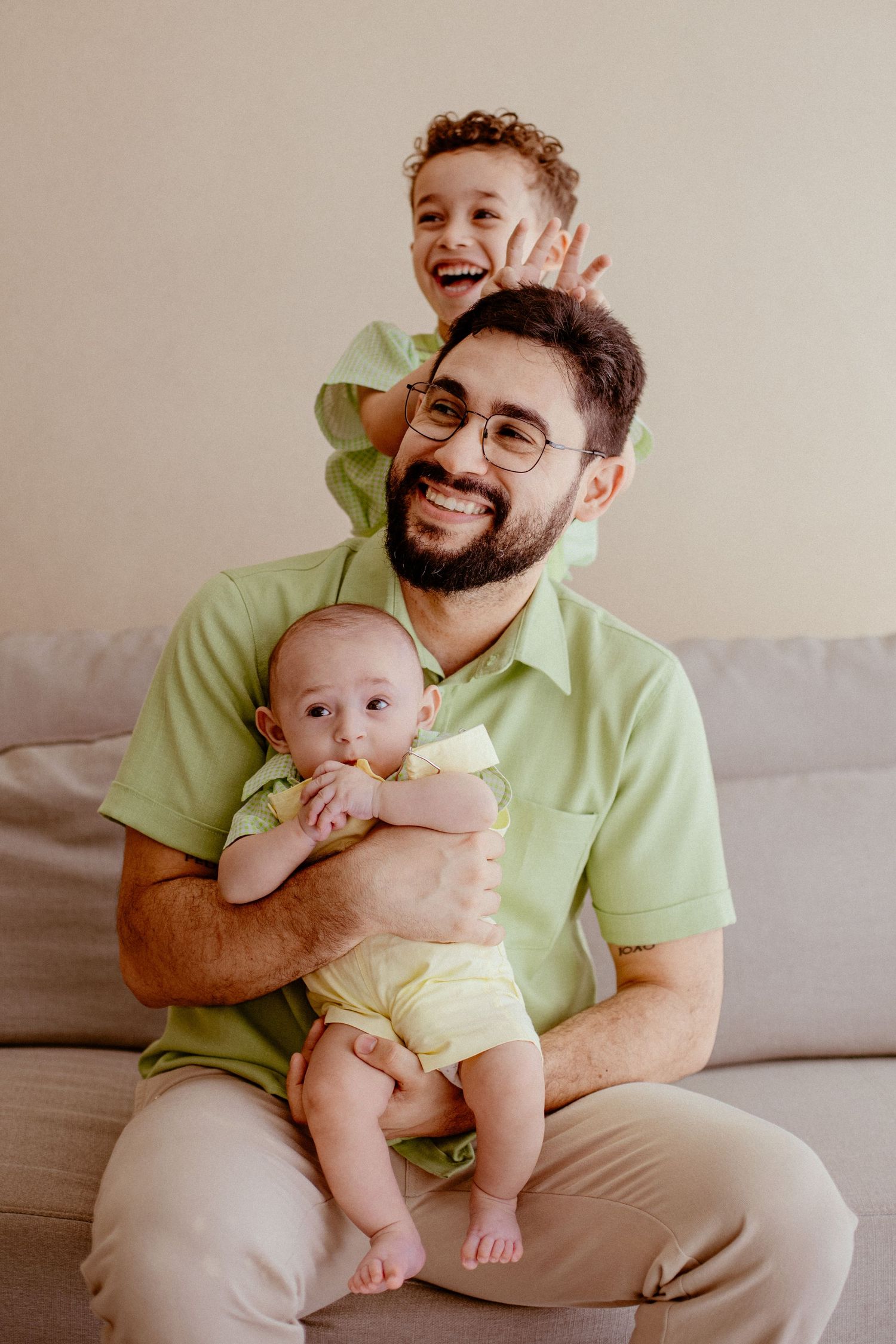 Happy family moment with father and children wearing matching green outfits sitting together on gray couch.