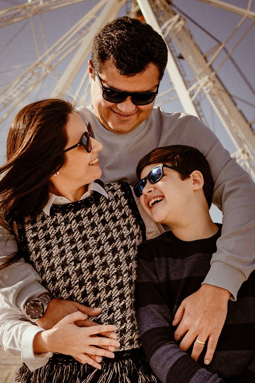 A happy family sharing a tender moment together while wearing sunglasses near a Ferris wheel structure.