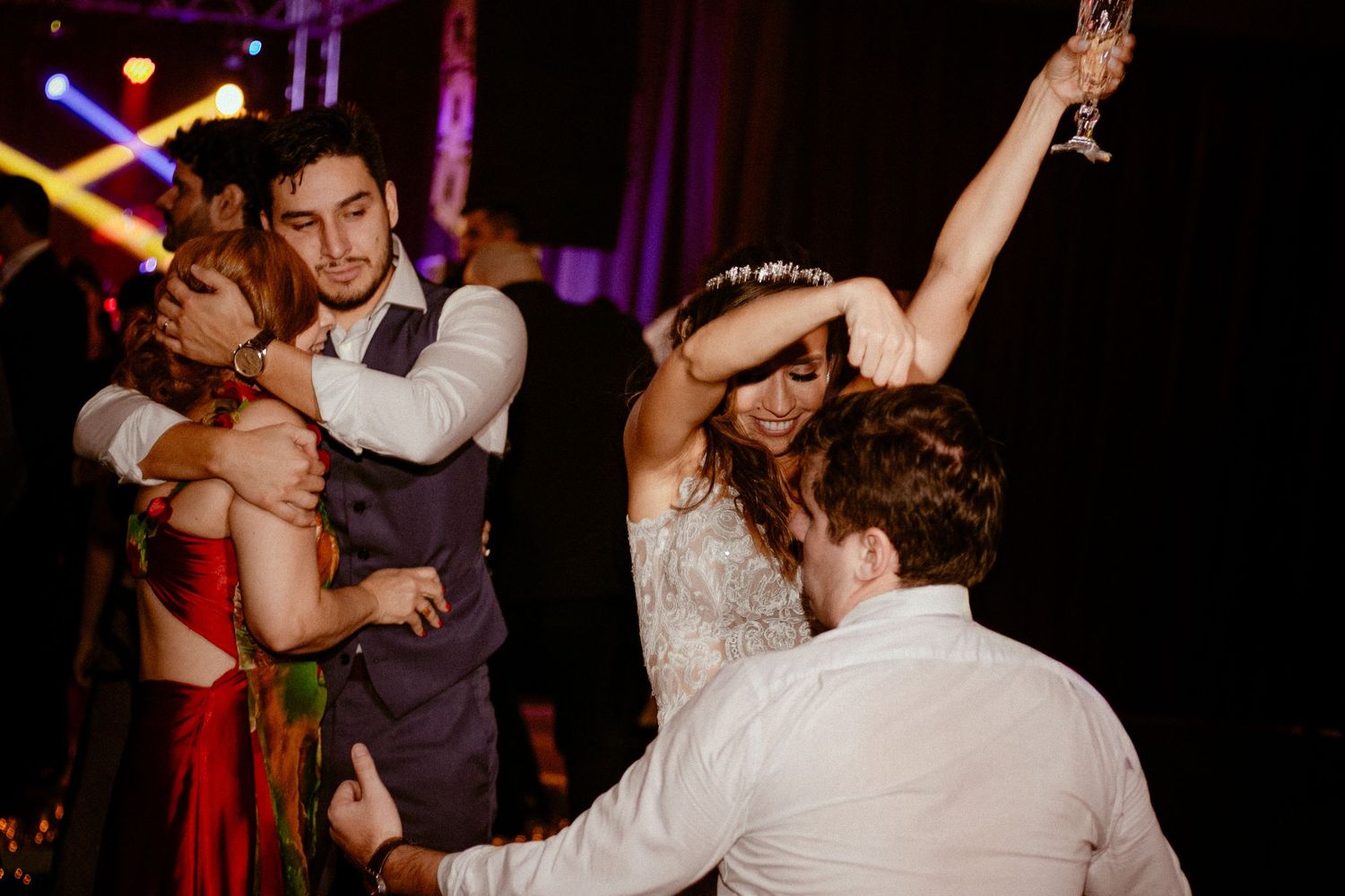 Wedding guests enjoying lively dancing and celebration on a dark dance floor with purple lighting.