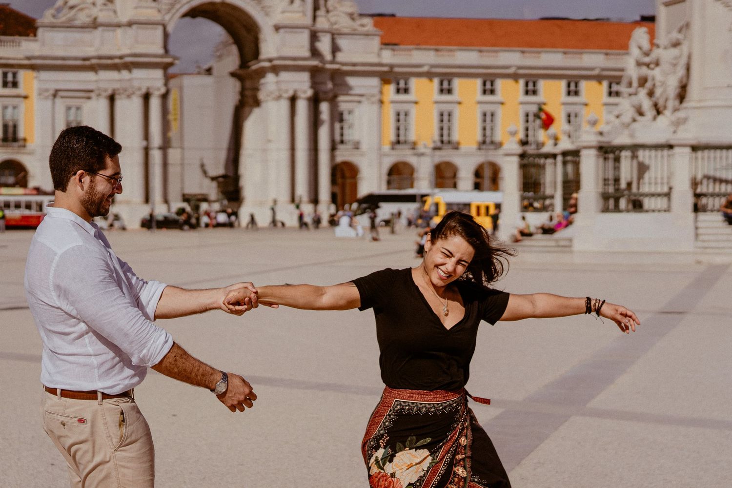 A couple performing a joyful dance sequence on a sunlit plaza with European architecture in the background.