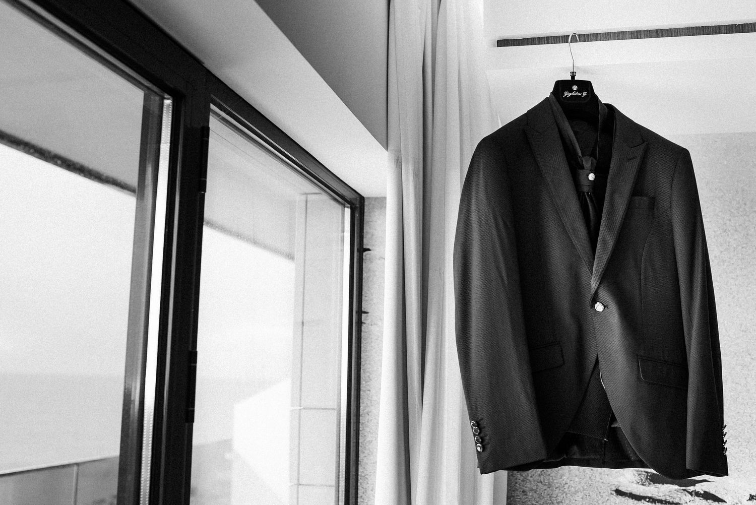 Black and white suits hang on hangers in a minimalist modern wardrobe display.