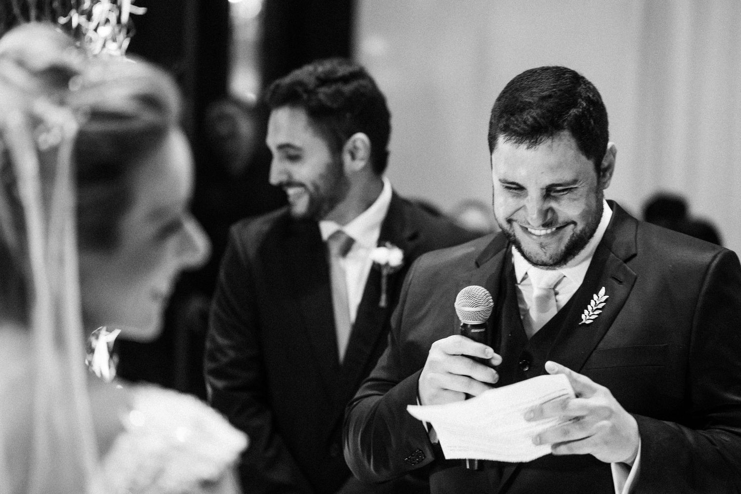 A candid black and white moment of laughter during wedding speeches.