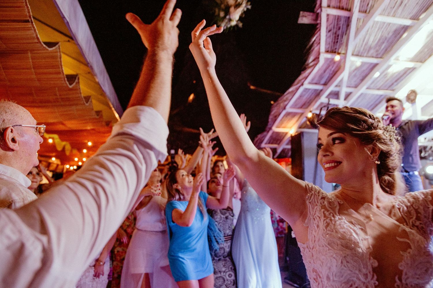Celebratory high-five between wedding attendees on a lively dance floor with colorful lighting and decorations.