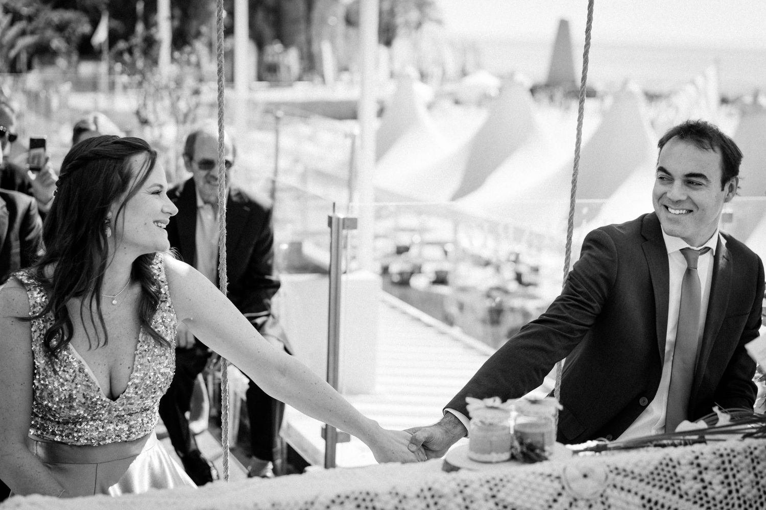 Wedding guests laughing and enjoying conversation at an outdoor reception table in black and white photography.