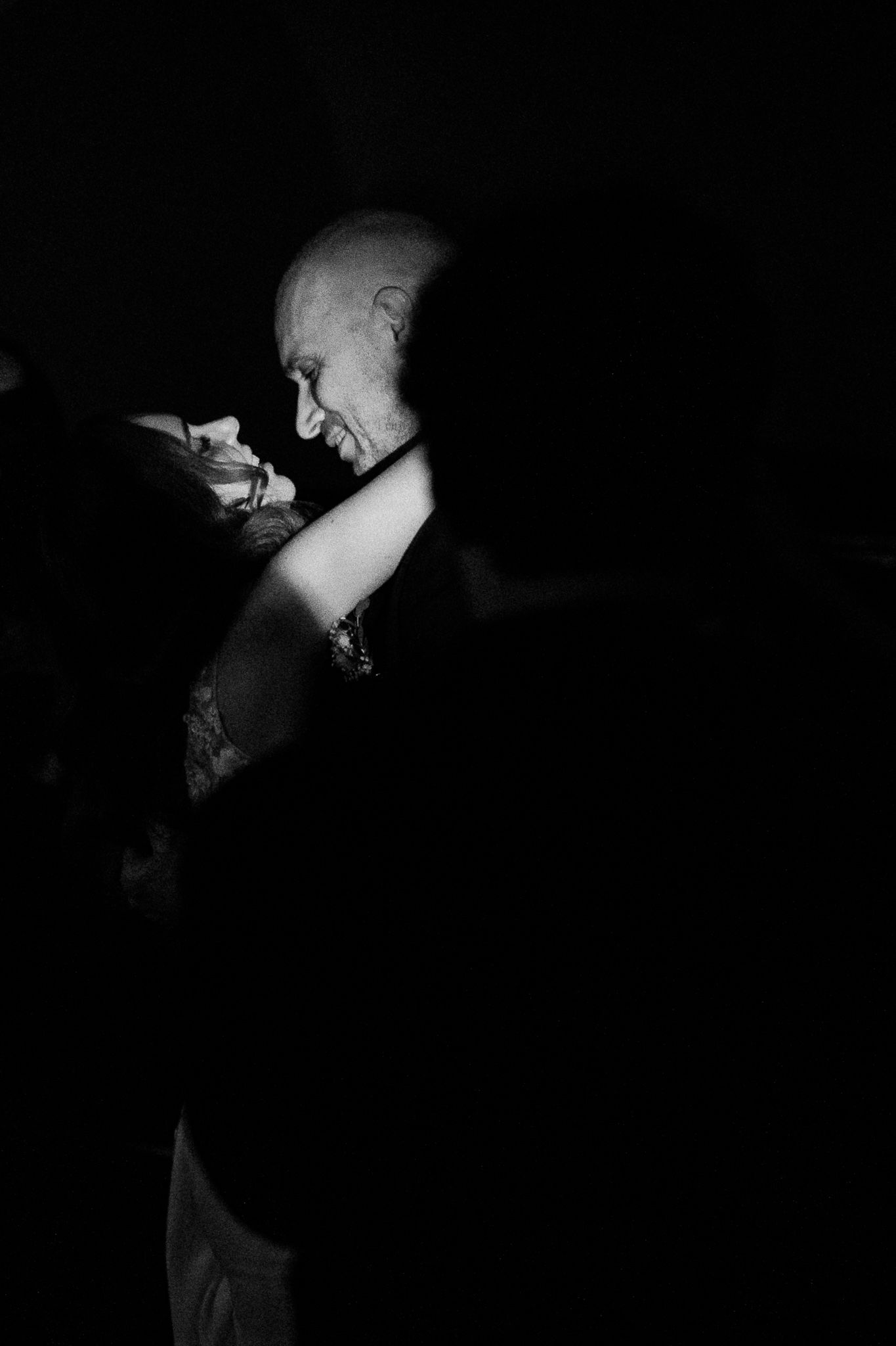 Elderly man dancing closely with a partner in a dramatic black and white wedding photo.