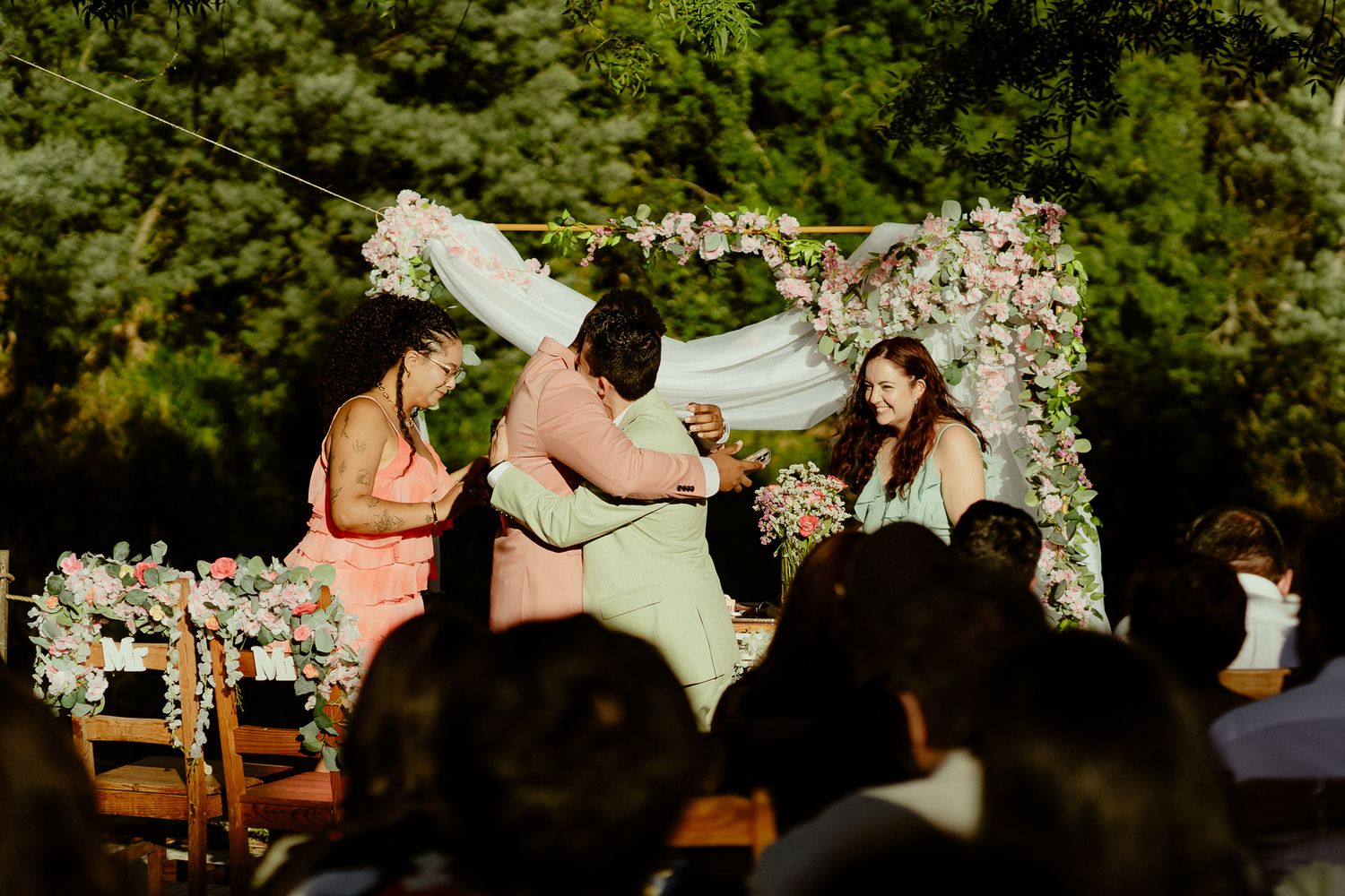 Outdoor wedding ceremony with officiant and couple under floral arch with pink flowers and white draping.